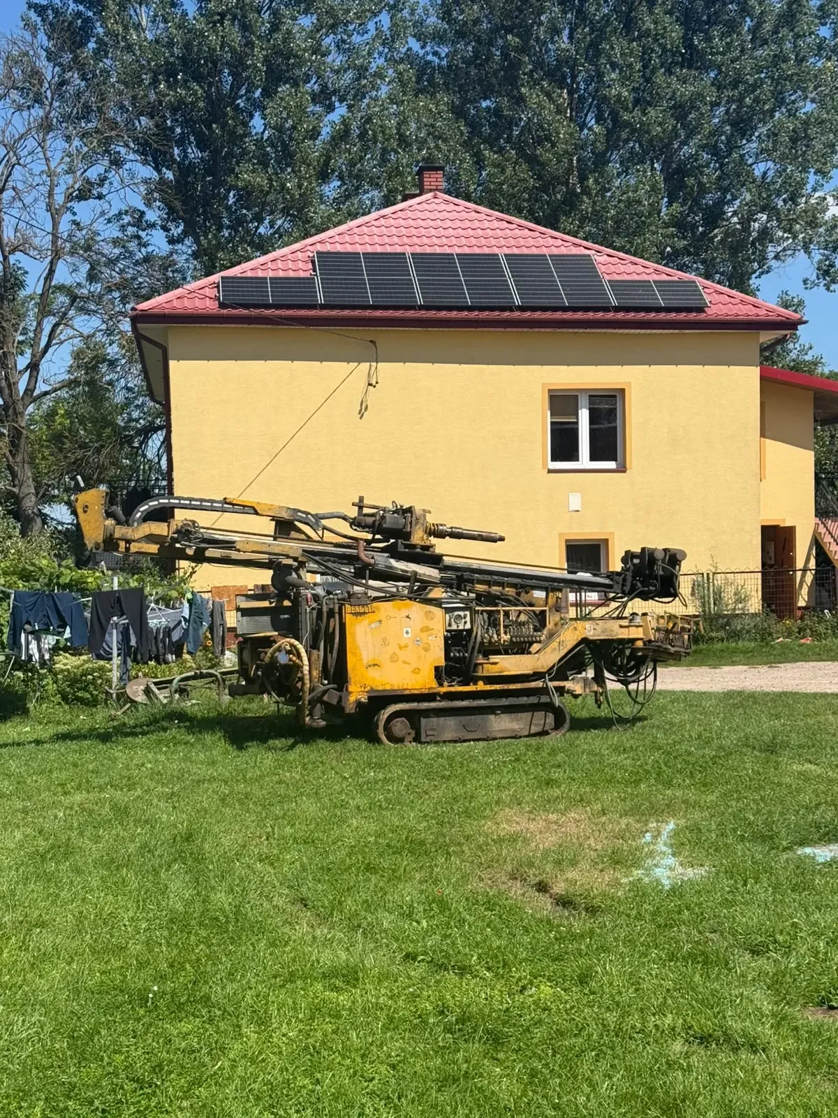 Żółta wiertnica gąsienicowa ustawiona na trawniku przed domem jednorodzinnym